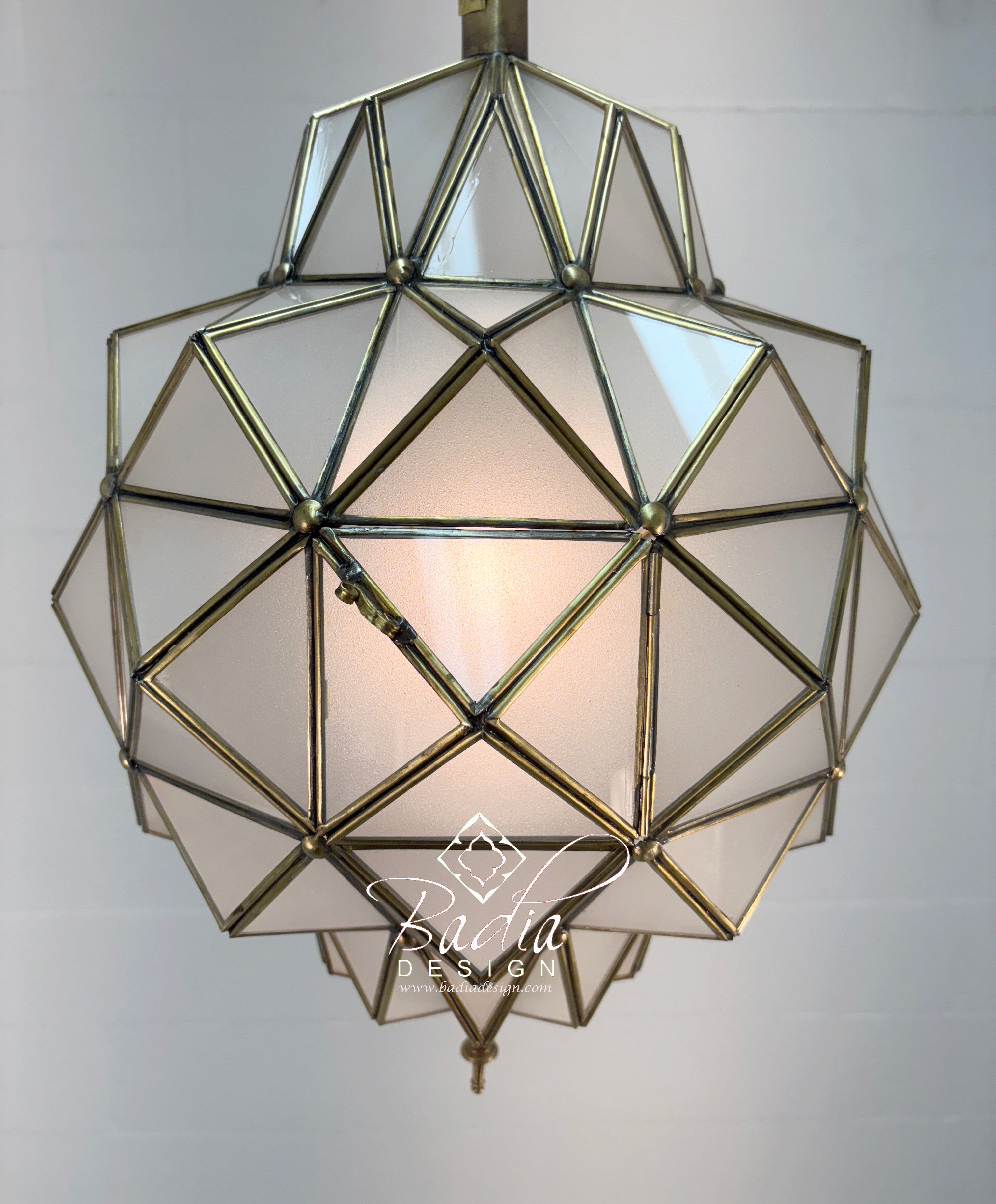 Geometric glass pendant light with brass frame on a plain background