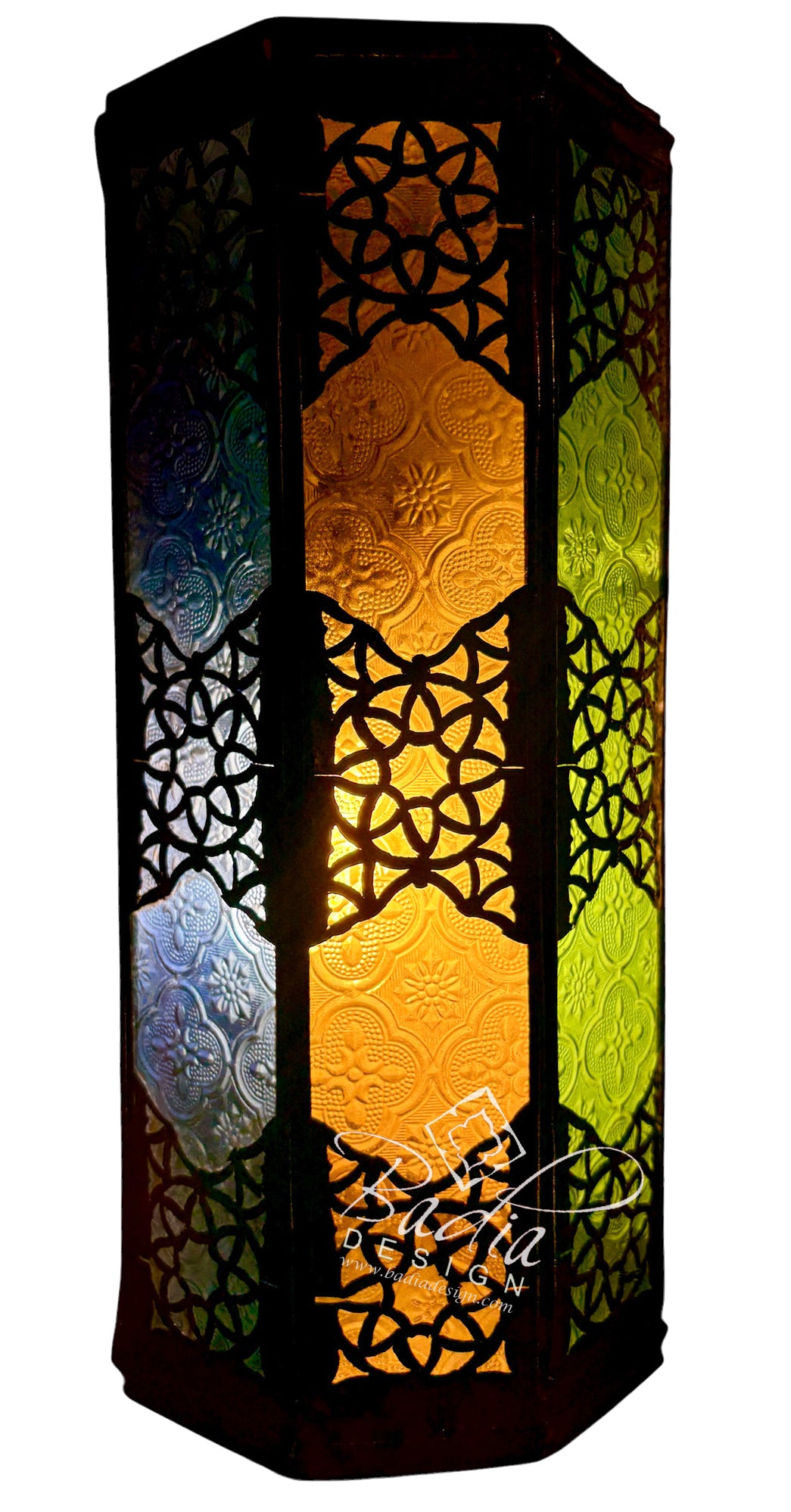 A tall, hexagonal Moroccan-style lantern with intricate black metal cutout patterns and illuminated stained glass panels in amber, yellow, green, and blue, shown against a plain white background.