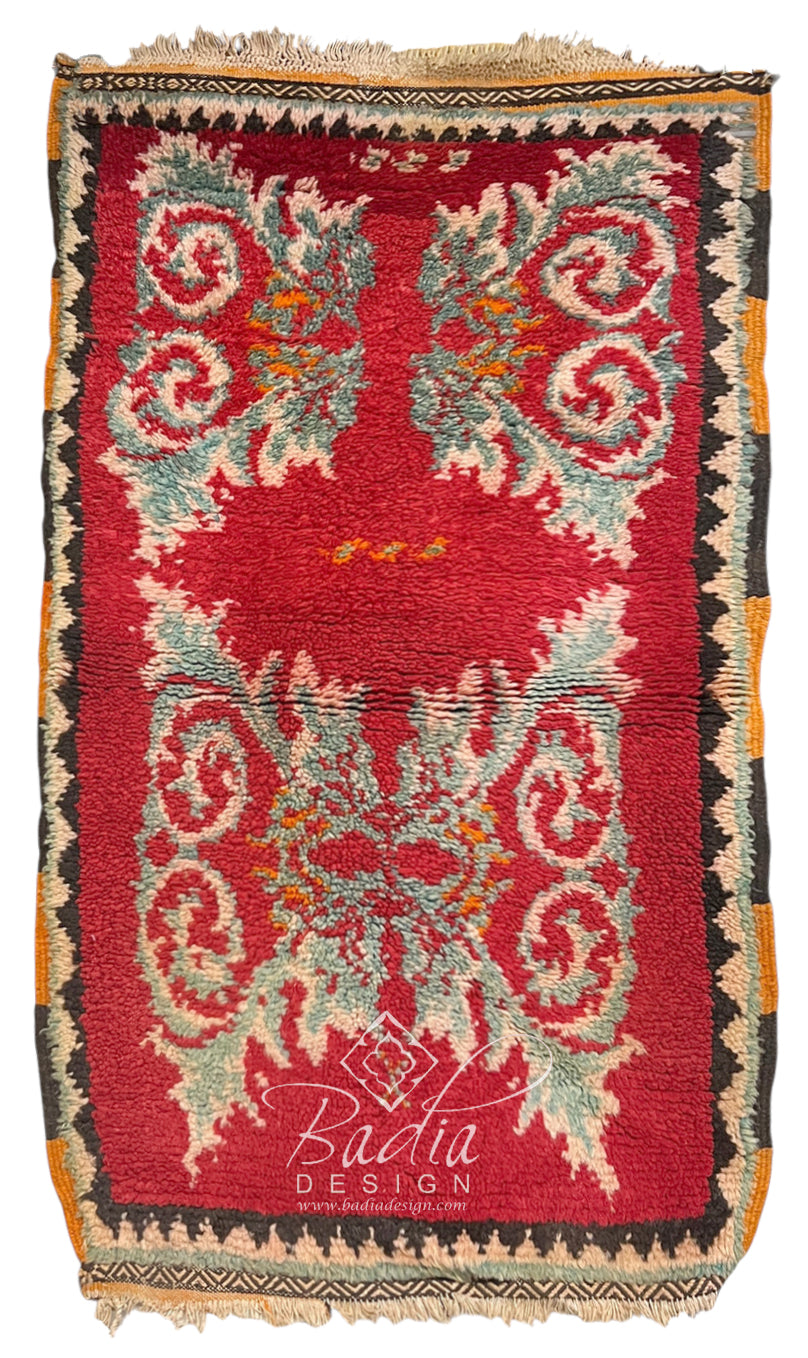 A rectangular vintage-style rug with a deep red field, ornate cream and light blue scroll motifs, and a dark border with orange and beige accents.