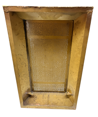 A rectangular brass radiator cover features an intricate laser-cut filigree pattern and sloped metallic sides.