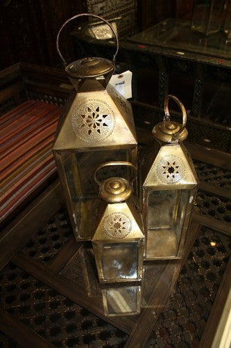 Two ornate brass lanterns on a reflective surface with a patterned background.