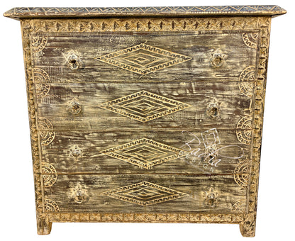 A distressed wooden chest of drawers with a weathered brown and beige finish, decorated with gold-toned geometric patterns and ornate drawer pulls.