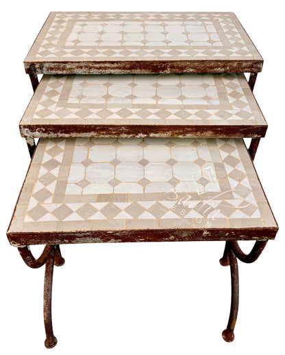A three-tier nesting side table with distressed brown metal frames and patterned mosaic tile tops in cream and beige, isolated on a white background.