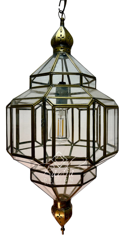 A hanging lantern-style pendant light with a brass or bronze metal frame and clear glass panels, shown against a plain white background. A bulb is visible inside, and a watermark/logo appears near the lower center.