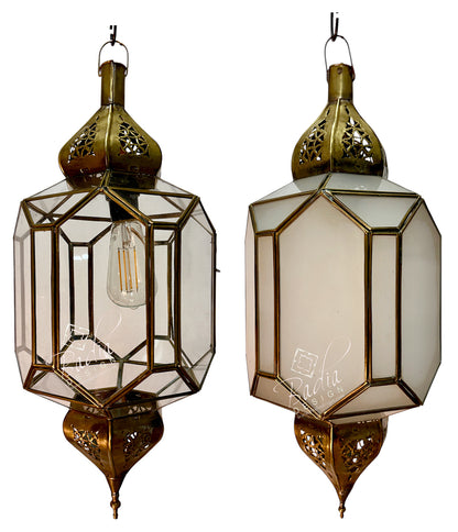 Two ornate hanging lanterns with brass-toned metal frames and clear glass panels, shown side by side against a white background. One lantern is open, revealing an exposed bulb, and the other is closed with a frosted or opaque inner panel.