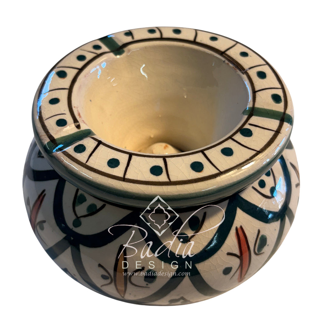 A round ceramic candle holder with a wide rim and a patterned base, featuring a cream interior and a multicolor hand-painted design in black, teal, and terracotta. A &