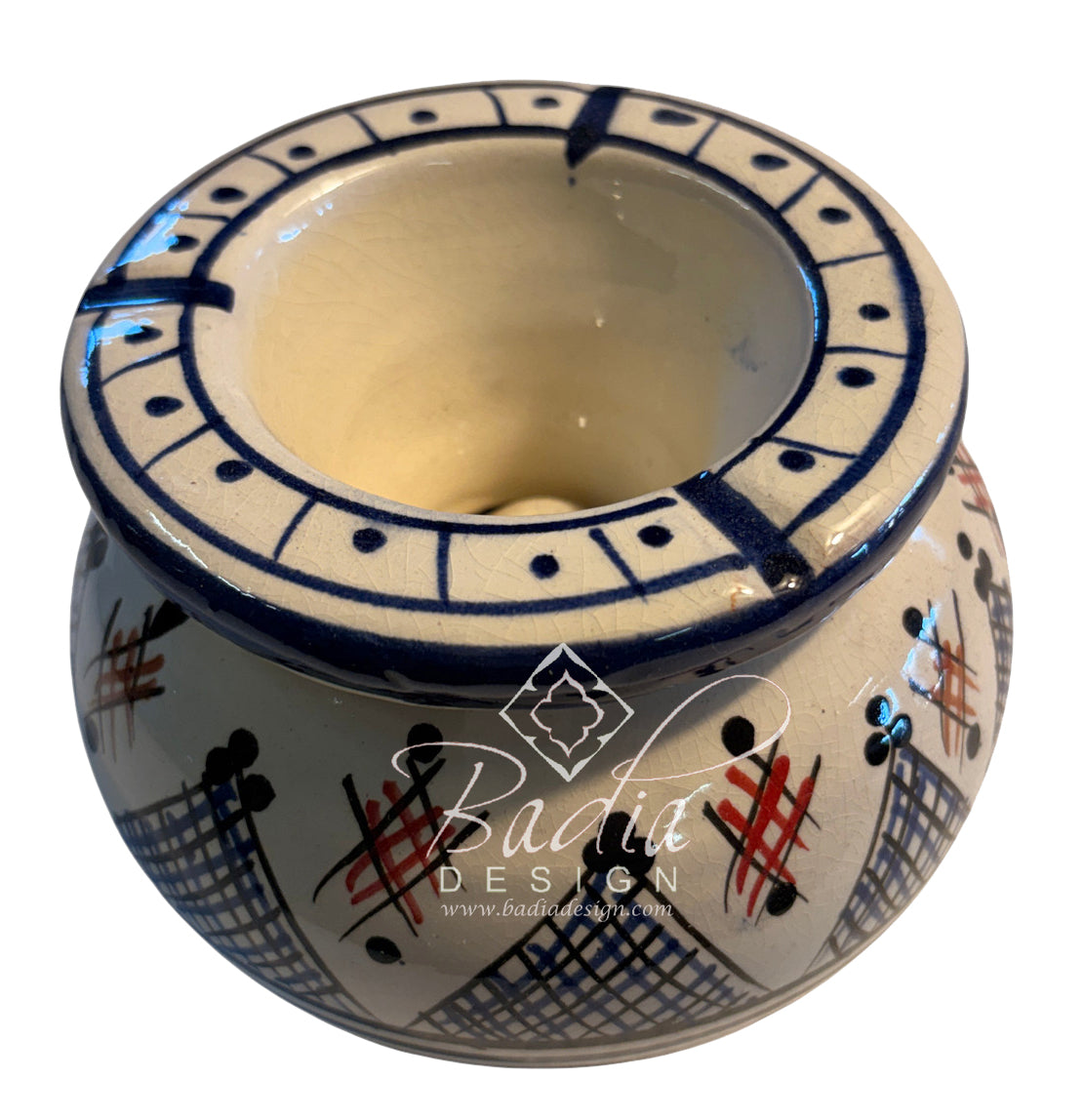 A handmade ceramic candle holder with a cream-colored glaze, decorated with blue geometric patterns, black crosshatch designs, and red accents. A &
