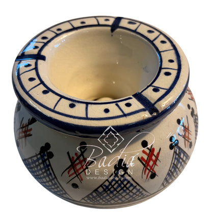 A handmade ceramic candle holder with a cream-colored glaze, decorated with blue geometric patterns, black crosshatch designs, and red accents. A &