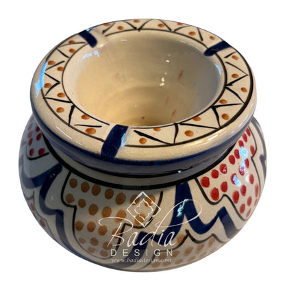 A hand-painted ceramic candle holder with a wide rim and a rounded base, decorated with blue, red, and orange patterns on a cream background. A &