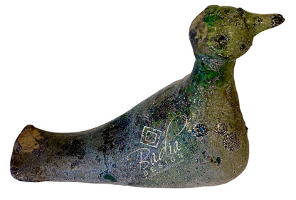 A rustic, handcrafted ceramic duck figurine with a textured, distressed finish in earthy green, brown, and gray tones, featuring a white script logo for &