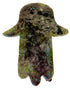 A Hamsa hand pendant made of polished Hessonite (molybdenite) featuring a rich, multicolored play of metallic green, gold, purple, and blue iridescence over a dark base. A watermark for &