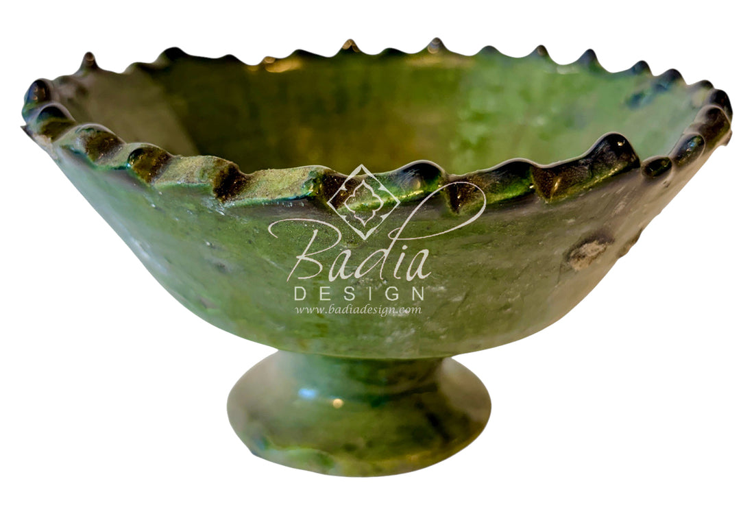 A green glazed ceramic pedestal bowl with a scalloped rim, shown against a plain white background with a &