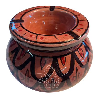 A small handmade ceramic pot with a terracotta orange-brown body, decorated with black geometric patterns and red accents, shown on a white background with a &