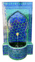 A Moorish-style mosaic tile fountain with a blue and green tiled arch, star pattern, and curved basin. A small gold-toned spout at the top releases a stream of water into the basin.