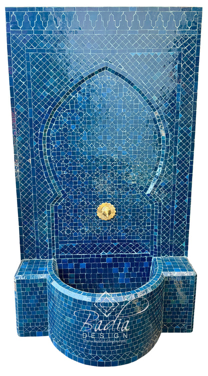 A blue mosaic fountain wall and basin with an arched niche, tiled in shades of blue with a small gold spout, shown on a white background.