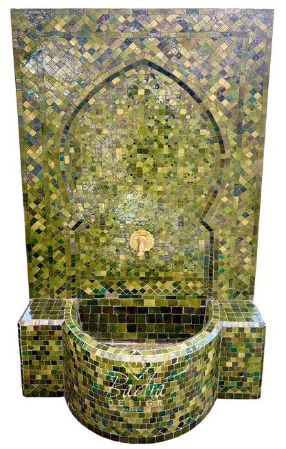 A Moorish-style mosaic tile fountain with a tall arched back panel and a curved basin, covered in green, olive, and gold-toned tiles with a small central spout.