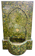 A Moorish-style mosaic tile fountain with a tall arched back panel and a curved basin, covered in green, olive, and gold-toned tiles with a small central spout.