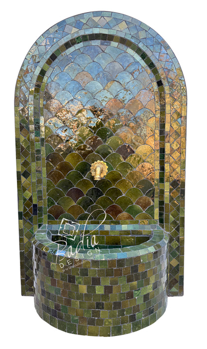 An arched mosaic fountain wall with a matching cylindrical basin, covered in reflective green, blue, and gold tiles. A small lion-head spout is centered near the top.