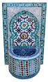A Moorish-style mosaic fountain wall and basin with intricate geometric tile patterns in turquoise, blue, white, green, and burgundy, featuring a central brass  spout.