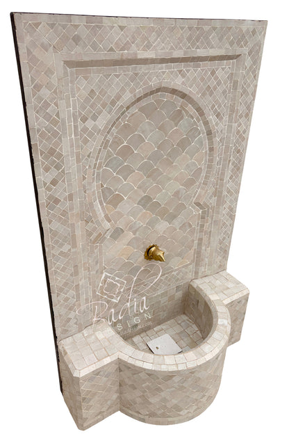 A Moroccan-style mosaic tile fountain wall basin with a curved recessed pool, scalloped tile arch, and a small gold-tone spout, shown on a plain white background.