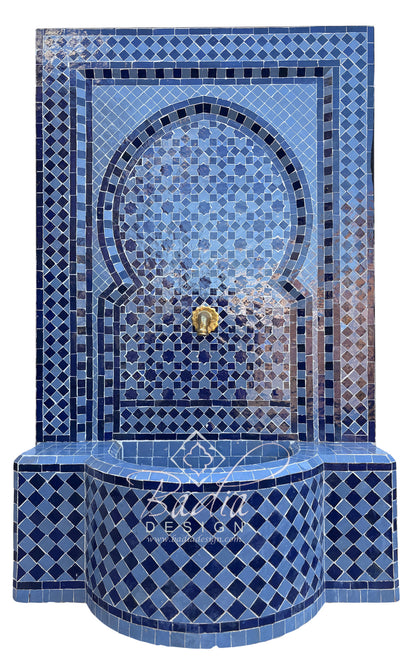 A Moorish-style mosaic tile fountain wall and basin in shades of blue, with a central gold-tone spout and a decorative script watermark reading &