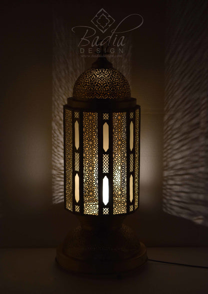 Decorative lamp with intricate patterns, illuminated in a dark setting, featuring the Badia Design logo.