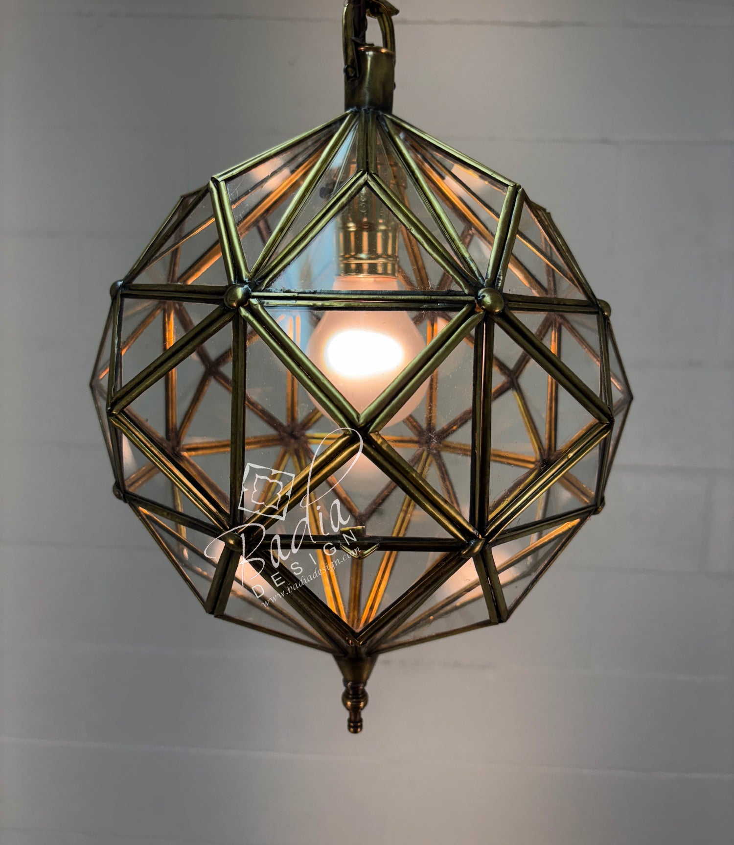 Geometric brass pendant light with clear glass on a plain background