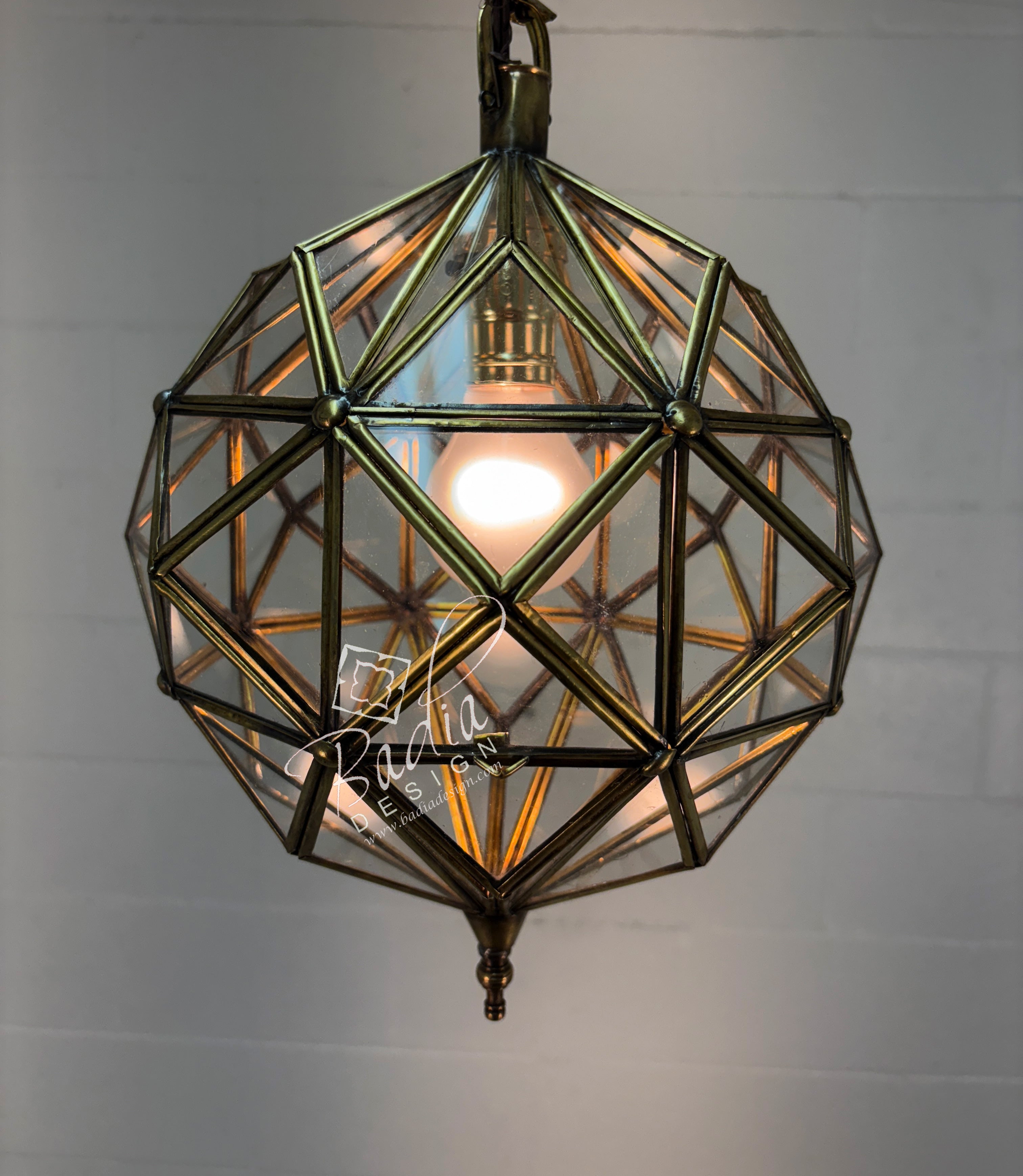 Geometric brass pendant light with clear glass on a plain background