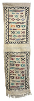 A long woven textile runner with two vertical panels featuring geometric and tribal-style patterns in black, red, blue, and orange on a cream background, finished with fringe at the bottom.