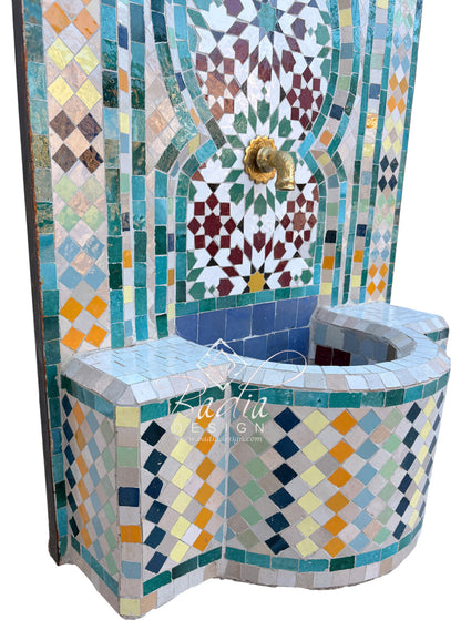 A Moroccan-style mosaic tile fountain with a curved basin, featuring intricate geometric patterns in blue, green, yellow, orange, and white, with a central gold-tone spout.