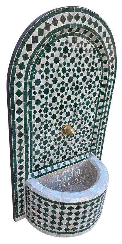 An arched Moroccan-style mosaic fountain wall with a matching curved basin, featuring green and white checkered tile patterns and a small brass spout.