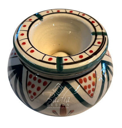 A hand-painted ceramic candle holder with a wide rim and a rounded base, decorated with geometric patterns in green, red, black, and cream. A &