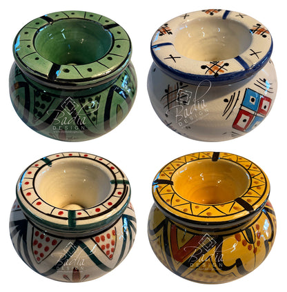 Four hand-painted ceramic candle holders arranged in a 2x2 grid, each with unique geometric patterns in green, blue, red, yellow, and black on white and cream backgrounds. A semi-transparent &