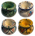 Four hand-painted ceramic candle holders arranged in a 2x2 grid, each with unique geometric patterns in green, blue, red, yellow, and black on white and cream backgrounds. A semi-transparent &
