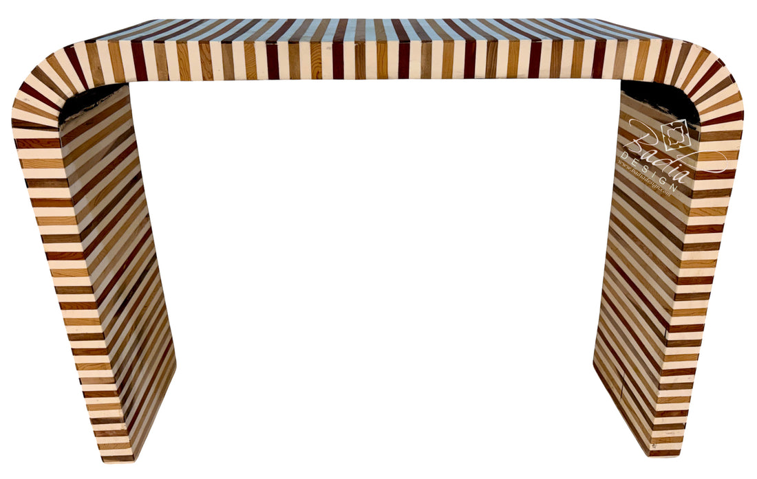 A modern console table with a curved top and legs, constructed from layered wood strips in alternating light tan, medium brown, and dark reddish-brown tones, shown against a plain white background.