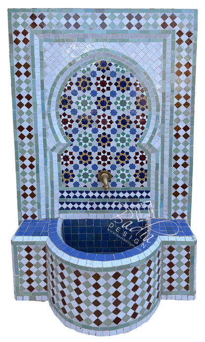 A Moroccan-style mosaic wall fountain with a curved tiled basin, decorative geometric patterns, and a central arch motif. The design features blue, green, white, brown, and gold tiles with a brass faucet at the top.