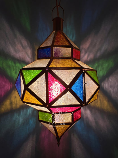 A hanging geometric stained-glass lantern with multicolored panels in blue, green, yellow, pink, and cream, casting colorful light patterns on a dark background. The brand name &