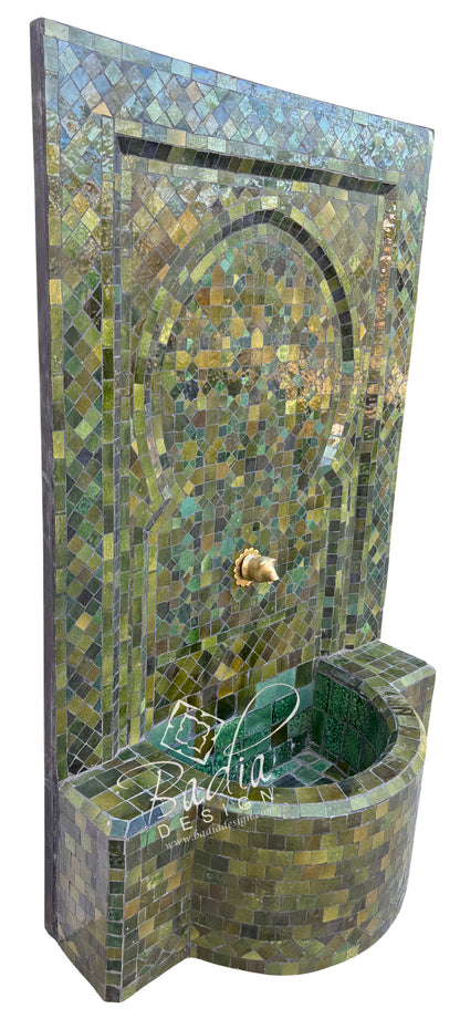 A mosaic wall fountain with a curved basin, covered in green, blue, and gold tile patterns, shown against a plain white background.