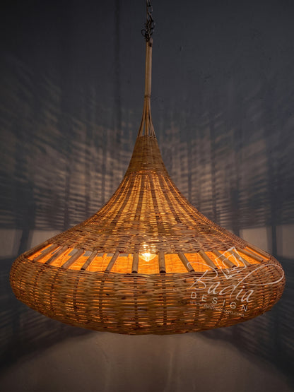 A large woven wicker pendant light fixture glowing with warm orange light, suspended against a dark gray wall with shadow patterns.
