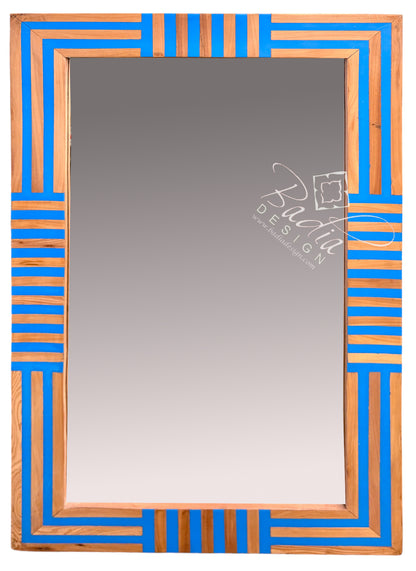 A rectangular wall mirror with a decorative geometric frame featuring alternating vertical stripes of bright blue and natural wood tones.