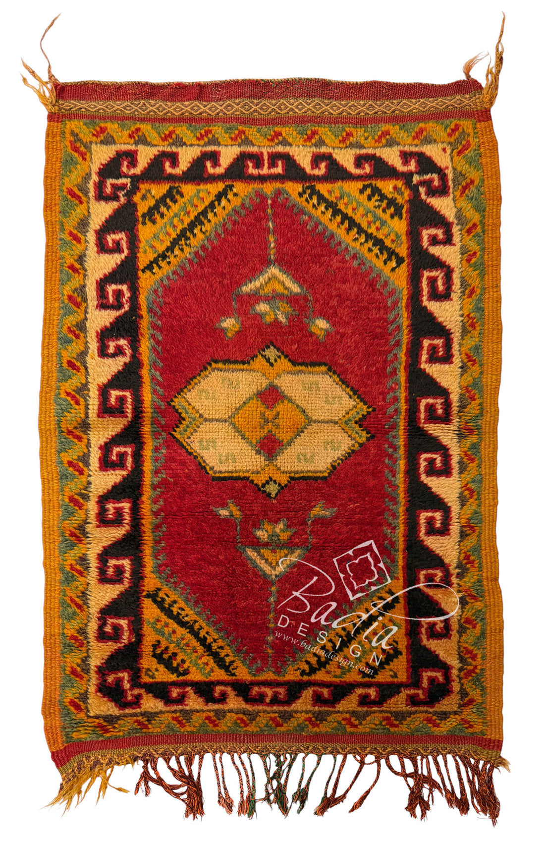A traditional handwoven rug with a red central field, geometric borders, and fringed edges, shown flat against a white background.