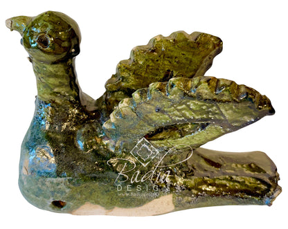 A handmade ceramic duck figurine with a textured, rustic finish, featuring a green and blue glaze over a beige clay base. The duck is shown from a side profile with wings spread, set against a plain white background with a &