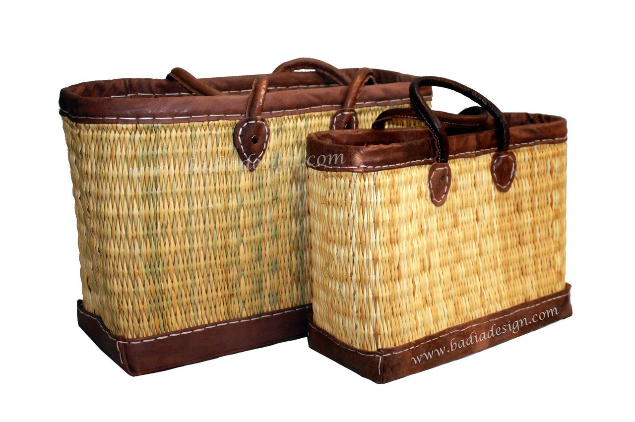 Two woven baskets with brown leather trim on a white background