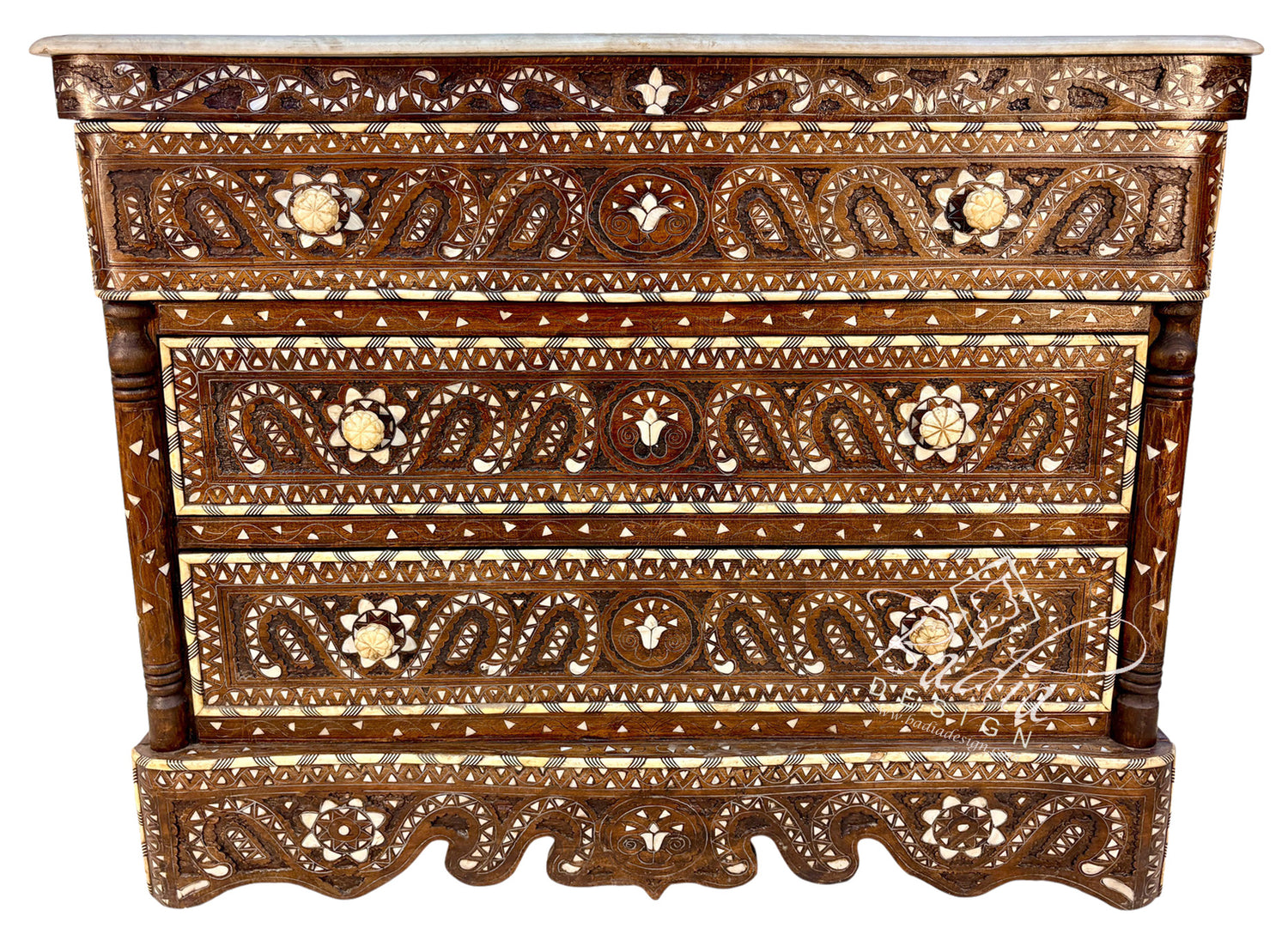 An ornate carved wooden chest of drawers with intricate mother-of-pearl inlays, featuring three drawers and a carved apron, shown against a plain white background.