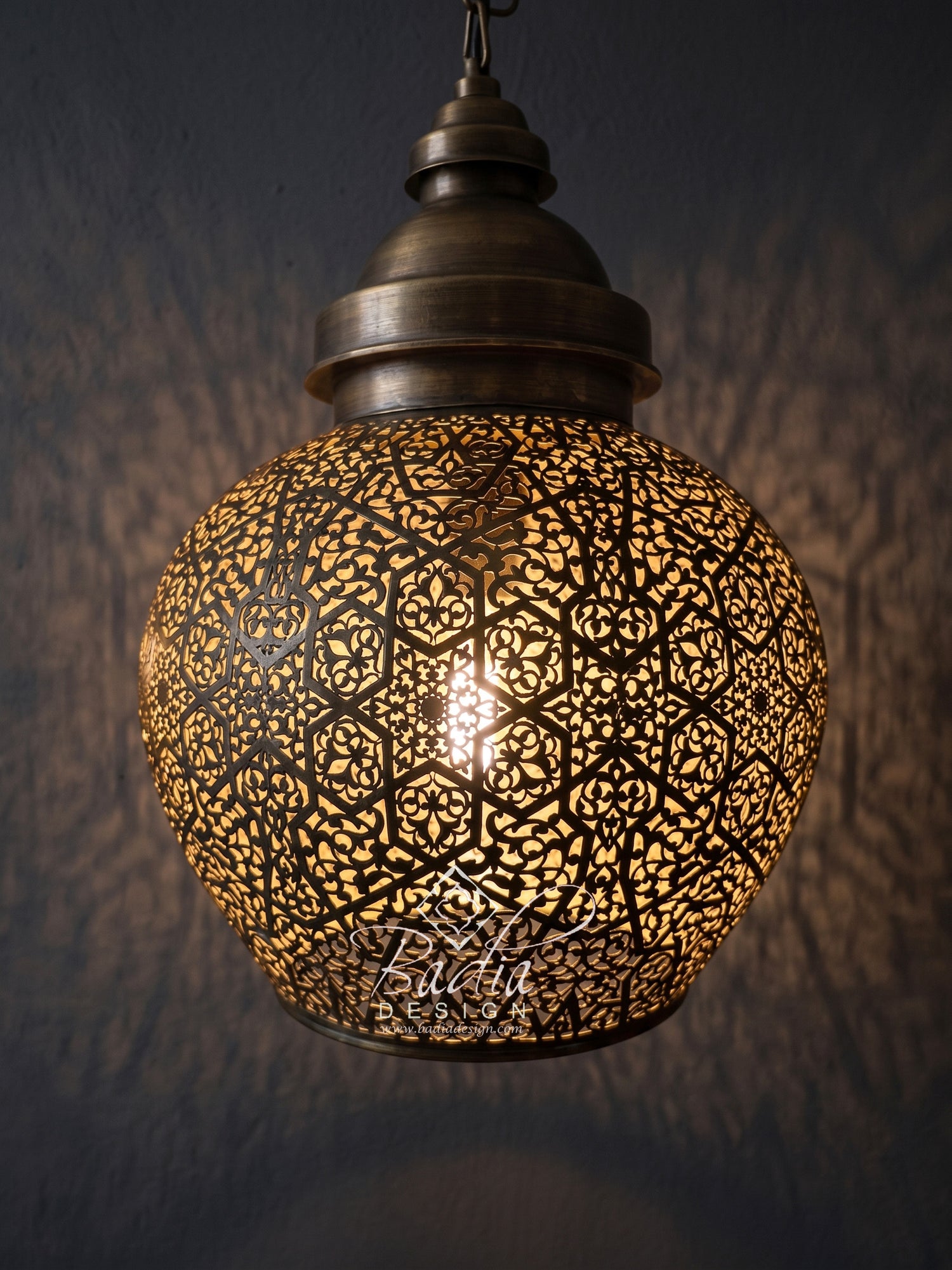 A spherical Moroccan-style pendant light with an intricate cutout metal shade, glowing with a warm light against a dark textured wall.