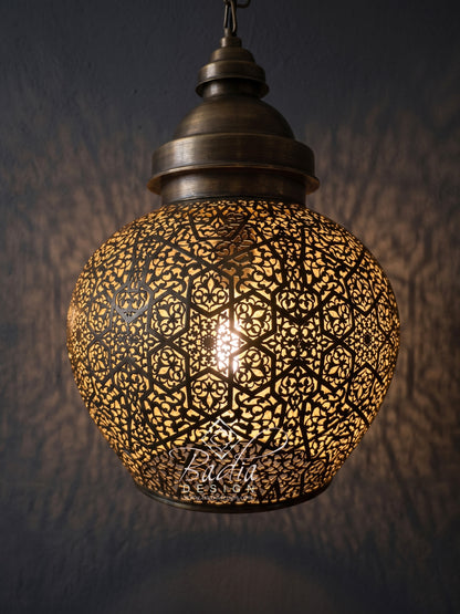 A spherical Moroccan-style pendant light with an intricate cutout metal shade, glowing with a warm light against a dark textured wall.