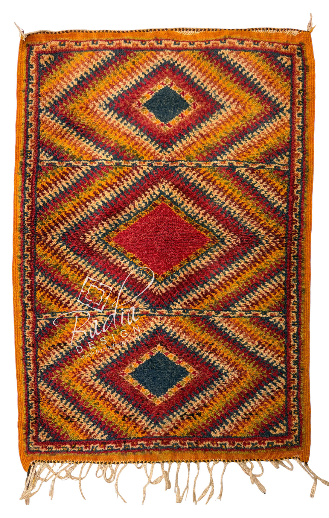 A rectangular hand-woven rug with a geometric diamond pattern in orange, red, yellow, and dark blue, featuring fringe along the bottom edge.