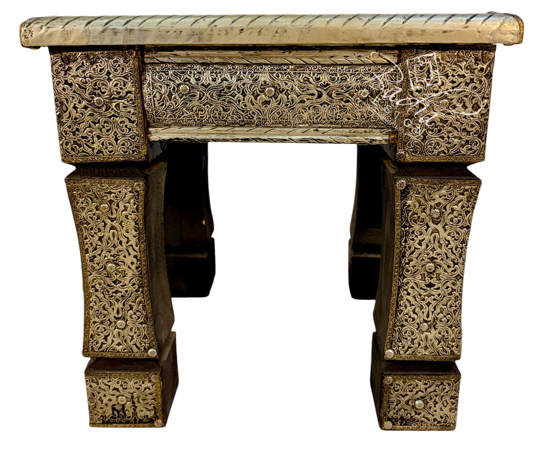 An ornate carved wooden table with intricate floral relief patterns on its legs and apron, featuring a light beige stone or plaster top, isolated on a white background.