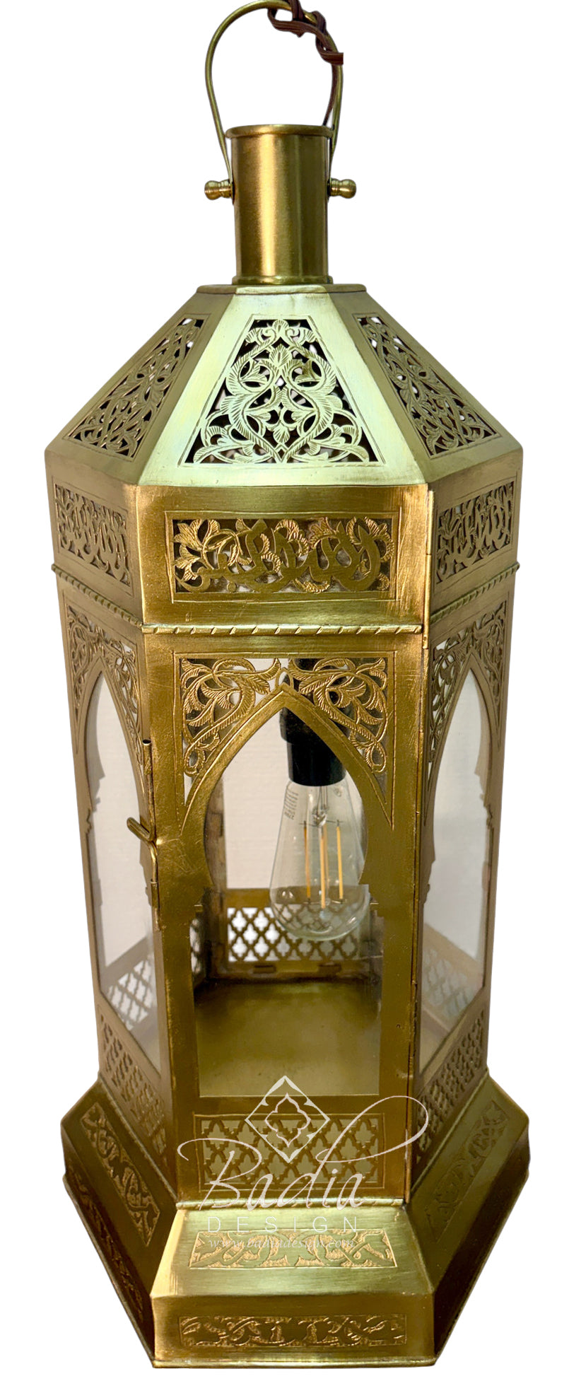 An ornate brass Moroccan lantern with intricate cutout patterns, clear glass panels, and a hanging loop at the top, shown against a plain white background.