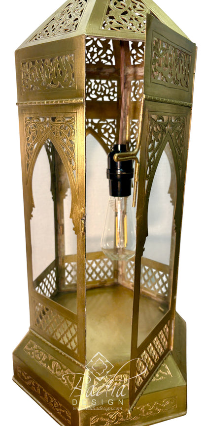 A brass Moroccan-style lantern table lamp with intricate cutout patterns, a clear glass bulb, and a black socket, shown on a white background.